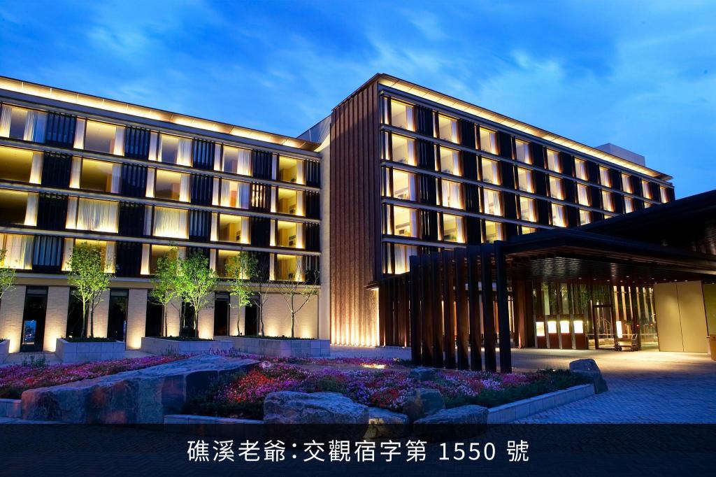礁溪老爺的入口夜景：深色木格柵立面、暖黃燈光，門前一整排小樹與紅花花圃