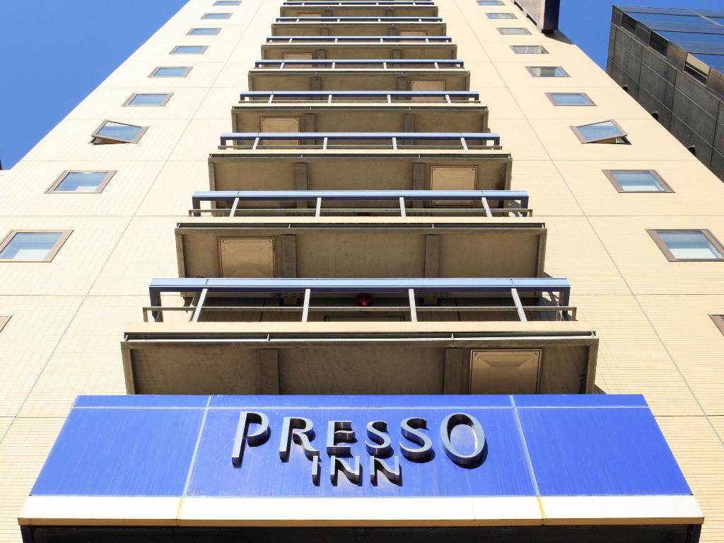 仰角拍白色磚牆的建築外觀,藍色雨遮上寫著 PRESSO INN,上方一排陽台欄杆一路往上延伸。