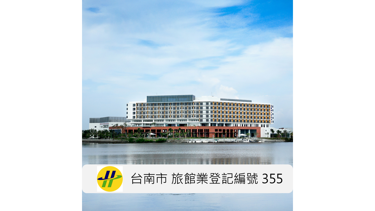 水岸邊的白色長形建築，低樓層是紅褐色基座，前方是一整片平靜的水面，天空是藍天配大片白雲。